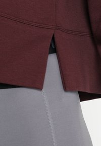 Haut bordeaux avec une finition texturée et une fente latérale, associé à des leggings gris ajustés avec un design sans couture et des coutures apparentes.