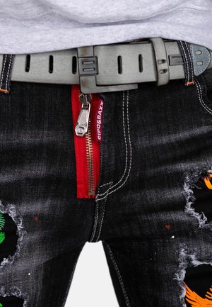 Zwarte denim broek met versleten plekken, rode ritsdetails en oranje en groene geborduurde patronen. Vergezeld van een grijze riem.