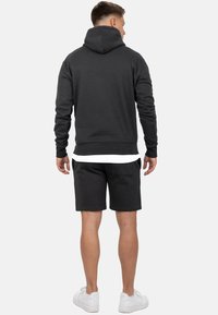 Donkergrijze hoodie met een kangoeroezak, gecombineerd met bijpassende shorts. Zachte stof, casual pasvorm en witte accenten op de schoenen.