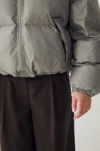 Γκρι μπουφάν με φερμουάρ μπροστά και ελαστικές μανσέτες που φοριέται με σκούρο καφέ παντελόνι, δείχνοντας το χέρι ενός ατόμου στο πλάι.
