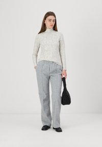 Light gray turtleneck with floral pattern, paired with loose-fitting gray trousers, holding a black textured bag, wearing black shoes.