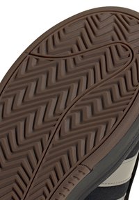 Nahaufnahme einer braunen Gummisohle mit Zickzackprofil und einer oberen Kante in Schwarz und Grau.