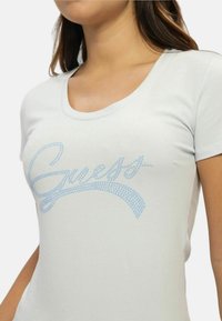 Lysegrå kortærmet t-shirt med blå rhinsten-logo design, rund halsudskæring og blød stofftekstur, tætsiddende til kroppen.