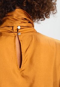 Sininen samettitoppi korkealla kauluksella, jossa on avainaukkoleikkaus selässä ja kaksi metallista nappia kiinnitystä varten.