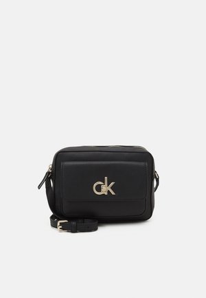 Sac bandoulière rectangulaire en cuir noir avec poche avant, logo CK doré, fermeture éclair dorée et sangle réglable avec boucle dorée.