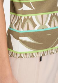 Ribbed, olive green top with multi-colored geometric patterns, featuring white and turquoise stripes and a gathered hem detail.