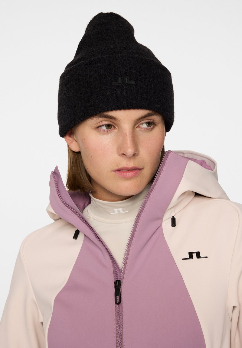 Berretto lavorato a maglia nero, giacca grigia e rosa con zip sopra una maglietta chiara. La giacca presenta chiusura a zip e dettagli con logo.