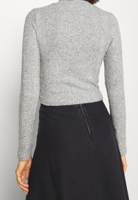 Graues geripptes Langarmoberteil mit hohem Kragen, kombiniert mit einem schwarzen Rock. Der Stoff ist weich und strukturiert und zeigt ein tailliertes Design.