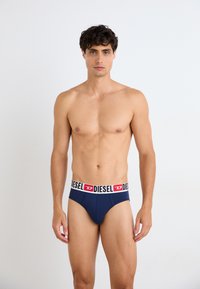 Marineblaue Herren-Briefsunterwäsche mit einem breiten elastischen Bund, der ein schwarzes und rotes "DIESEL"-Logo trägt, glatter Textur und taillierter Passform.
