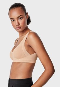 Sujetador inalámbrico beige con escote en V, tirantes anchos y una textura suave y lisa. Diseño ajustado, costuras mínimas y sin aros.