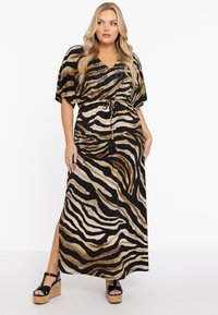 Robe maxi noire, marron et beige à rayures de tigre avec un col en V, des manches courtes et une taille à cordon réglable. Présente une fente sur le côté.