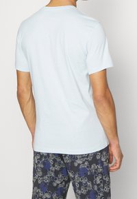 T-shirt bleu clair à manches courtes avec un col rond, texture douce en coton, porté avec un pantalon sombre à motifs présentant des designs floraux bleus et gris.