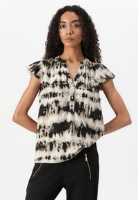 Løs, kortermet bluse i svart og kremfarget tie-dye mønster, med knappestolpe og volanger på ermene, laget av lett stoff.