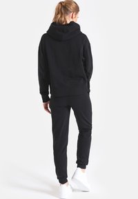 Czarna bluza z kapturem o luźnym kroju, zestawiona z pasującymi spodniami dresowymi. Materiał wydaje się miękki, z prążkowanymi mankietami i ściągaczami.