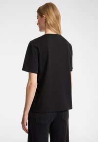 Camiseta negra de manga corta hecha de algodón, con un ajuste relajado, escote redondo y textura suave, vista desde la parte posterior.