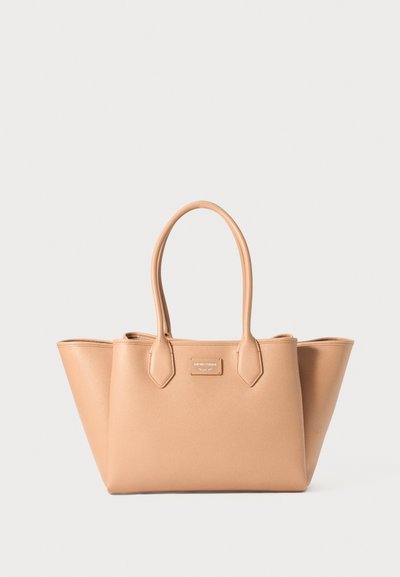 Torebka tote z syntetycznego materiału w kolorze tan z dwoma pionowymi uchwytami, o sztywnej formie i gładkiej fakturze. Posiada metalową płytkę z logo z przodu.