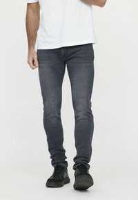 Graue, taillierte Jeans aus Denim mit klassischem 5-Taschen-Design und leichten Verwaschungen an der Vorderseite. Kombiniert mit schwarzen Sneakers.