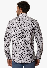 Camisa blanca con patrón circular negro, con un cuello clásico y mangas largas, hecha de una tela ligera. Se muestra la vista trasera.