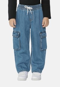 Modré denimové cargo kalhoty s elastickým pasem, bílým šňůrkou a dvěma velkými bočními kapsami. Spárovány s bílými teniskami.