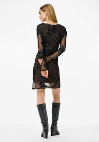 Juoda nėrinių suknelė su gėlių siuvinėjimu, permatomomis ilgomis rankovėmis ir apvalia iškirpte. Derinama su juodais, iki kelių siekiančiais aukštakulniais batais su platforma.