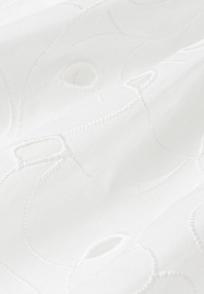 Material alb cu broderie complexă, detalii decupate, textură netedă și un luciu subtil, evidențiind modele de design pe întreaga suprafață.