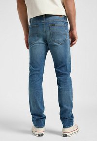 Moške modre denim hlače s slim fit krojem, z zadnjimi žepi, svetlimi madeži in kontrastnim šivanjem, v kombinaciji z belimi supergami.