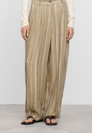 Pantaloni beige a gamba larga con righe bianche verticali abbinati a sandali neri con punta quadrata e top crema a maniche lunghe.