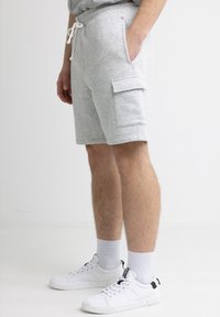 Grau mélange Baumwollshorts mit elastischem Bund und Kordelzug, ausgestattet mit Seitentaschen und einer Cargotasche am Oberschenkel, kombiniert mit weißen Turnschuhen.