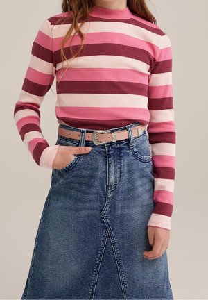 Person iført en langærmet top med pink, burgundy og hvide striber, stukket ind i et denimskørt med et lyserødt bælte.