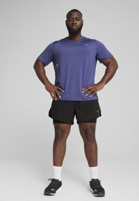 Lilla atletisk T-shirt med korte ærmer, der har et lille logo. Sorte shorts, hvide sokker og sorte atletiske sko fuldender sættet.