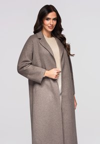 Grijze wollen jas met een reverskraag, lange mouwen en een rechte snit. Draagt over een crème trui, met een gladde, gestructureerde afwerking.