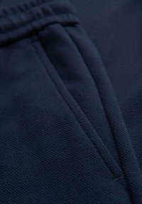 Gros plan sur un tissu texturé bleu marine avec une couture repliée et une ouverture de poche, mettant en valeur les détails de couture et de matériau.