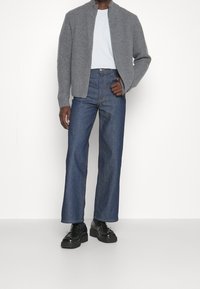 Grå ribbade cardigan, ljusblå t-shirt, vida mörkdenim jeans och svarta snörskor med tjocka sulor och metallaccenter.