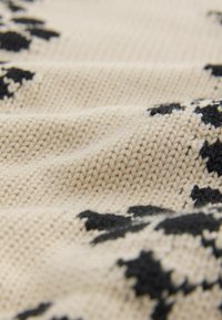 Tissu tricoté en crème avec un motif d'étoiles noires, présentant une surface texturée et un fil lisse. Le gros plan montre les détails du tissage.