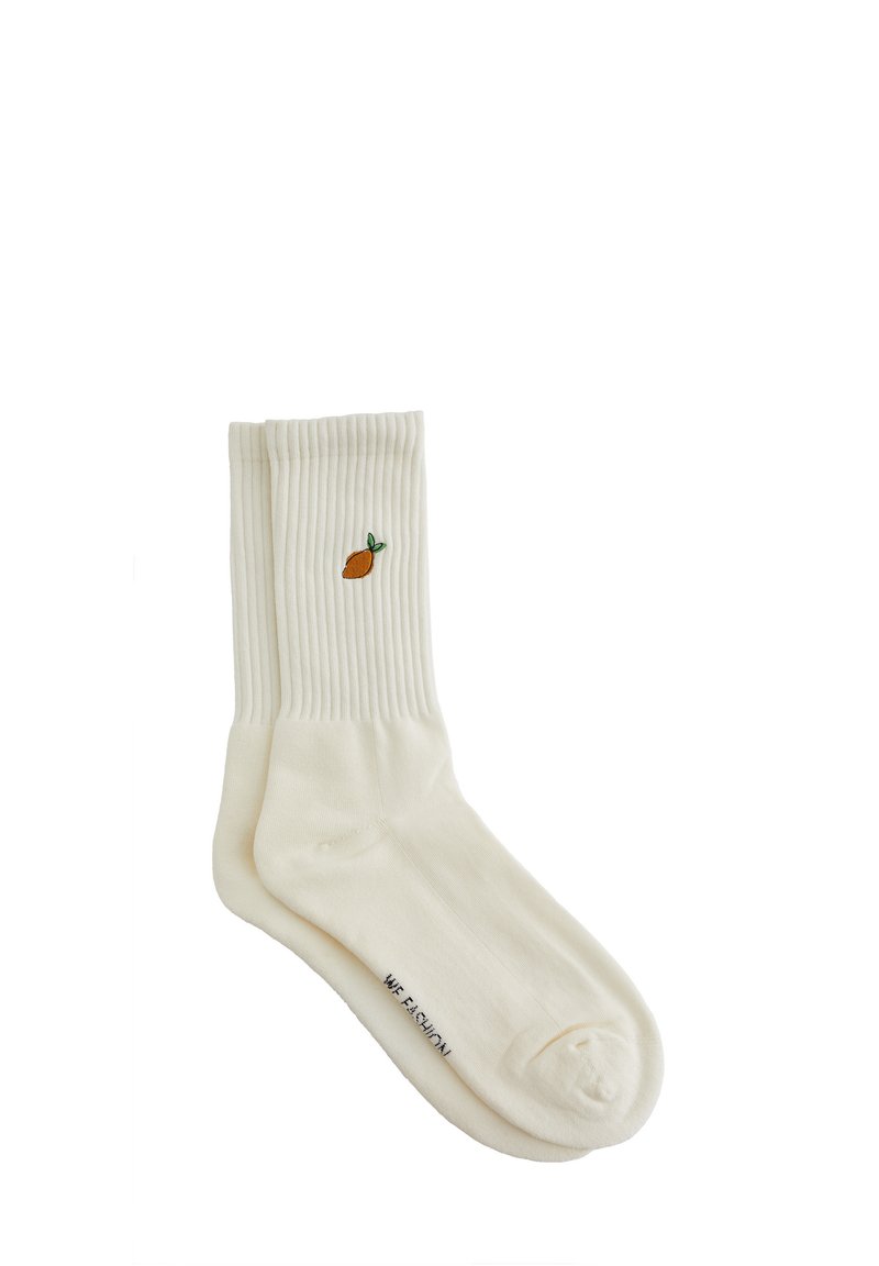 Vita ribbade bomullssockor med en broderad apelsin och ett grönt blad på sidan. Tyget är mjukt med en slät textur.