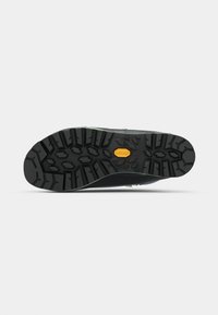 Fekete gumitalp mély barázdákkal, Vibram logóval és zöld díszítéssel a széleken, amely a tapadást és a tartósságot jelzi.