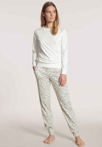 White long-sleeve top paired with lightweight pajama pants featuring a spotted pattern in beige and black. Soft fabric, elastic cuffs.
