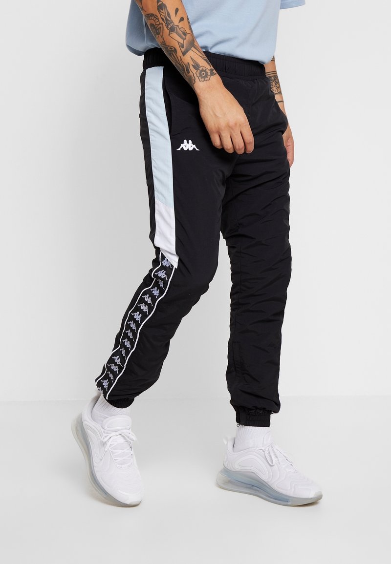 Svarta vadderade joggers med ljusblå och vita sidopaneler, med en logotyp och ett mönstrat accentband som går längs med vänster ben. Elastisk midja.