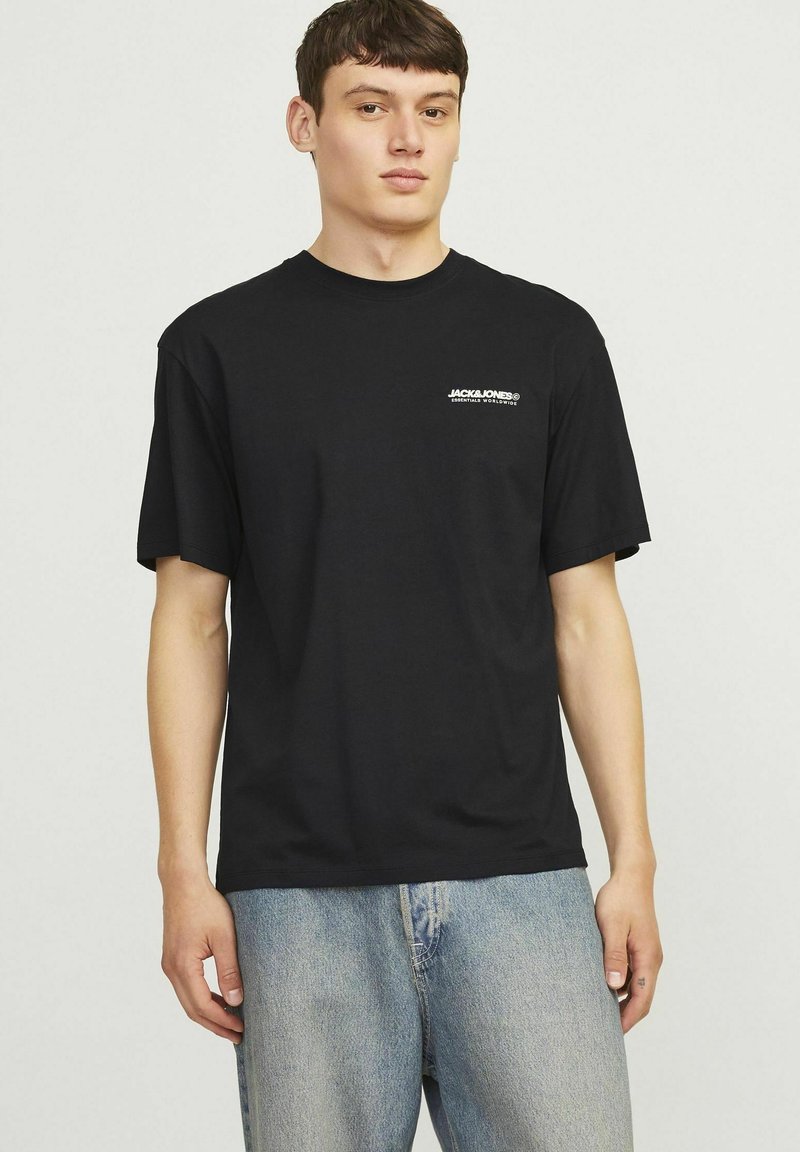 Sort bomuld t-shirt med korte ærmer, rund halsudskæring og et hvidt logo på venstre bryst. Matchet med lyseblå denim jeans.