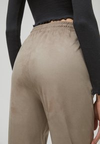 En person bär en kroppsnära svart long-sleeve topp och löst sittande beige byxor, med fokus på klädernas textur och midjeresår.