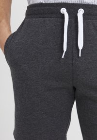 Pantalons de survêtement gris foncé avec une texture douce, dotés d'une taille élastique et de cordons blancs. Poches latérales incluses.