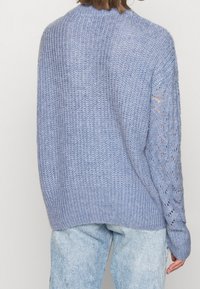 Maglione blu oversize a maglia con texture a coste e motivo a intaglio sulle maniche, abbinato a jeans in denim chiaro.