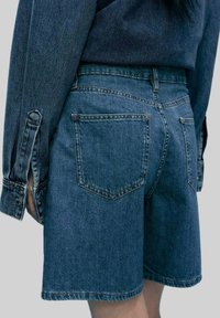 Shorts en denim bleu foncé, avec une coupe classique, deux poches arrière et des coutures détaillées sur la taille et les ourlets.