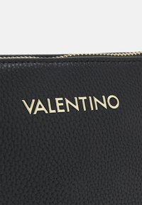 Pochette en cuir noir avec une finition texturée et le logo doré "VALENTINO". Fermeture éclair avec quincaillerie dorée sur le dessus.