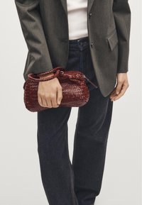 Woven red leather handbag with a rounded shape and two handles. Features a zip closure and a textured pattern on the surface.