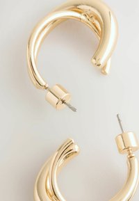 Orecchini a cerchio in metallo dorato con un design liscio e curvo. Presentano un perno e un supporto per una vestibilità sicura, evidenziando una finitura lucida.