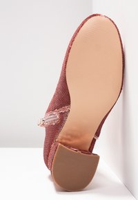 Chaussure en tissu mauve unique inclinée pour montrer la semelle beige lisse et le petit talon bloc contre un arrière-plan blanc en coin.