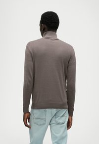 Pruuni, pikkade varrukatega pullover-sviiter kõrge kraega ja siledast materjalist, kantud helesiniste teksadega, millel on tagataskud.