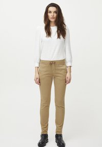 Top blanco de manga larga ligero y texturizado, combinado con pantalones khaki ajustados con cintura elástica y bolsillos laterales, usados con botas negras de tobillo.