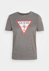 Šedé bavlněné tričko s krátkým rukávem a kulatým výstřihem. Obsahuje velké červené logo ve tvaru trojúhelníku s nápisem "GUESS" a bílým designem otazníku.